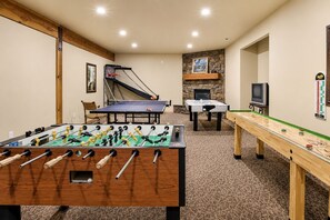 Una habitación con mesa de fútbol de mesa, mesa de ping pong, mesa de fútbol de mesa con chimenea de piedra y mesa de shuffleboard.