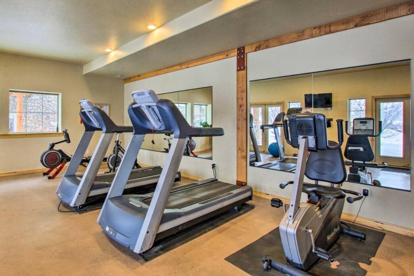 Un gimnasio con cintas de correr, bicicletas estáticas y un espejo grande.