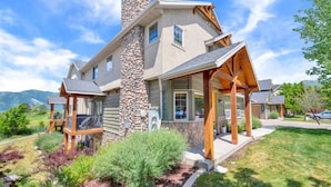 A two-story house with a stone chimney, wooden porch, and a landscaped front yard. - Eden Basecamp | w/Pool, Hot Tub, + Sauna (Eden)