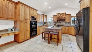 A spacious kitchen with wooden cabinets, a central island with stools, a refrigerator, and a microwave. - Eden Basecamp | w/Pool, Hot Tub, + Sauna (Eden)