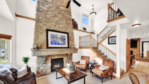 A spacious living area with a stone fireplace, a wooden staircase, and a cozy seating arrangement. - Eden Basecamp | w/Pool, Hot Tub, + Sauna (Eden)