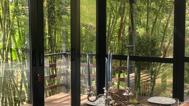 A dining area with a long table set for a meal, large windows, and a view of greenery. - Beautiful House With Views To The Reservoir And Wonderful Waterfalls. (El Peñol)