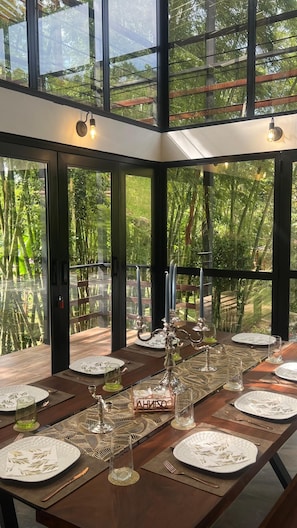 Comedor con una larga mesa dispuesta para una comida, ventanas amplias y vista a zonas verdes.