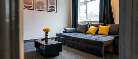 A modern living room with a sofa, a coffee table, and a window with curtains.