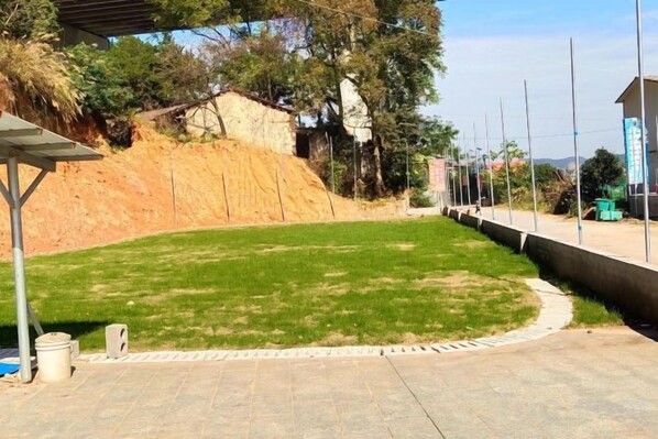 Un área pavimentada con un pequeño sector de césped, un muro de concreto y una cerca de metal.