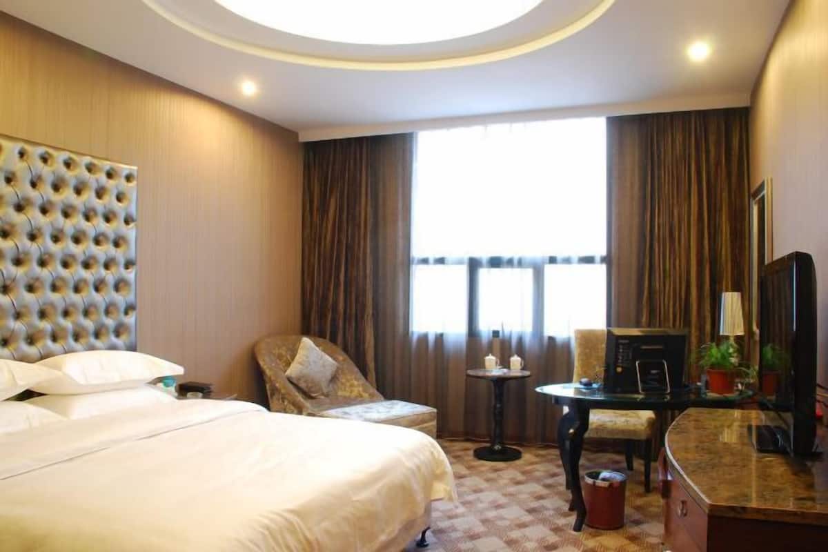 Ein Hotelzimmer mit einem großen Bett, einer Couch, einem Schreibtisch mit Computer und einem Fenster mit Vorhängen.