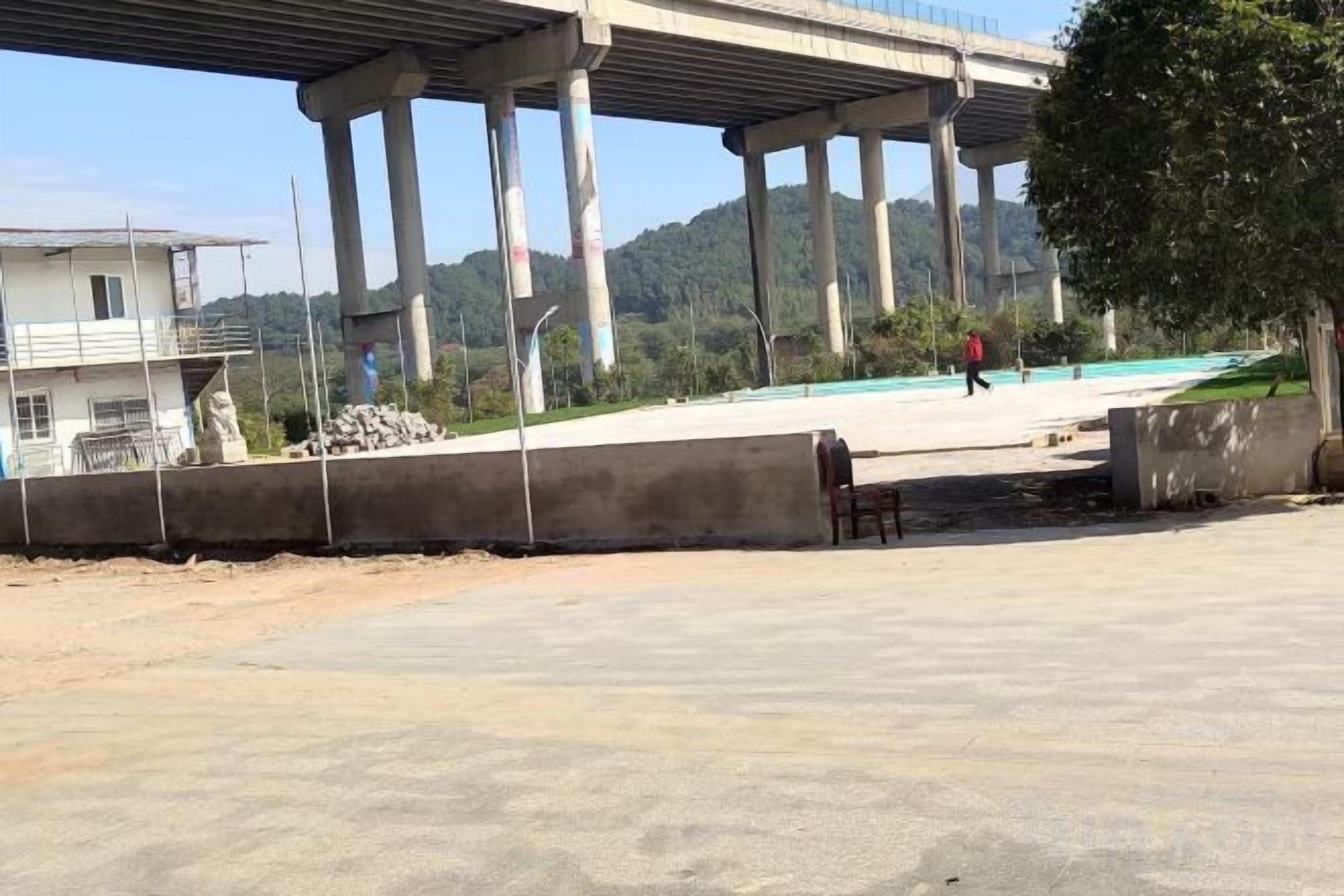 A concrete area with a bridge overhead, a person walking, and a building in the background.