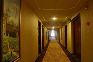 Um corredor de hotel com portas, piso coberto de carpete e um mural na parede esquerda.