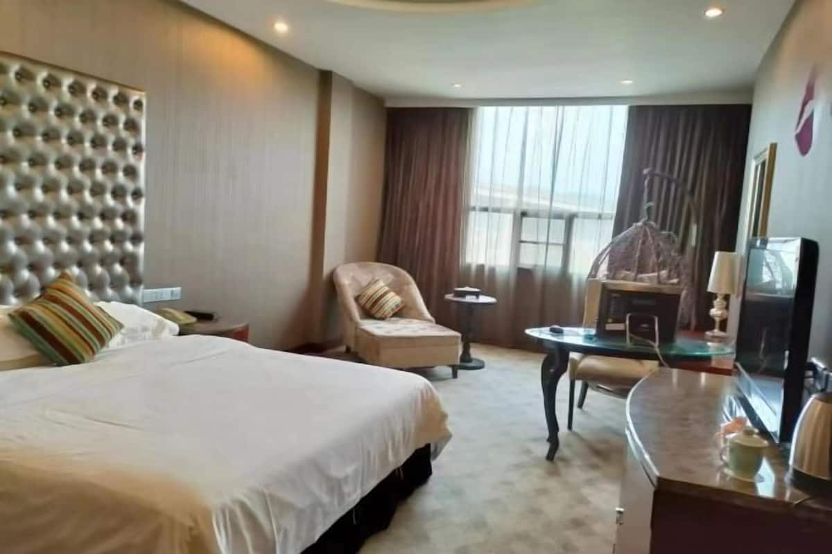 Ein Hotelzimmer mit einem großen Bett, einem Sessel, einem Schreibtisch und einem Fernseher.