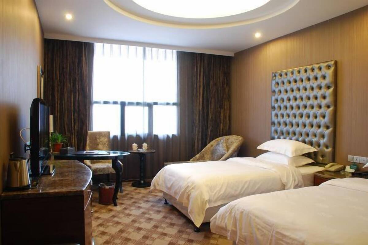Ein Hotelzimmer mit zwei Betten, einem Fernseher, einem Schreibtisch und einem großen Fenster mit Vorhängen.
