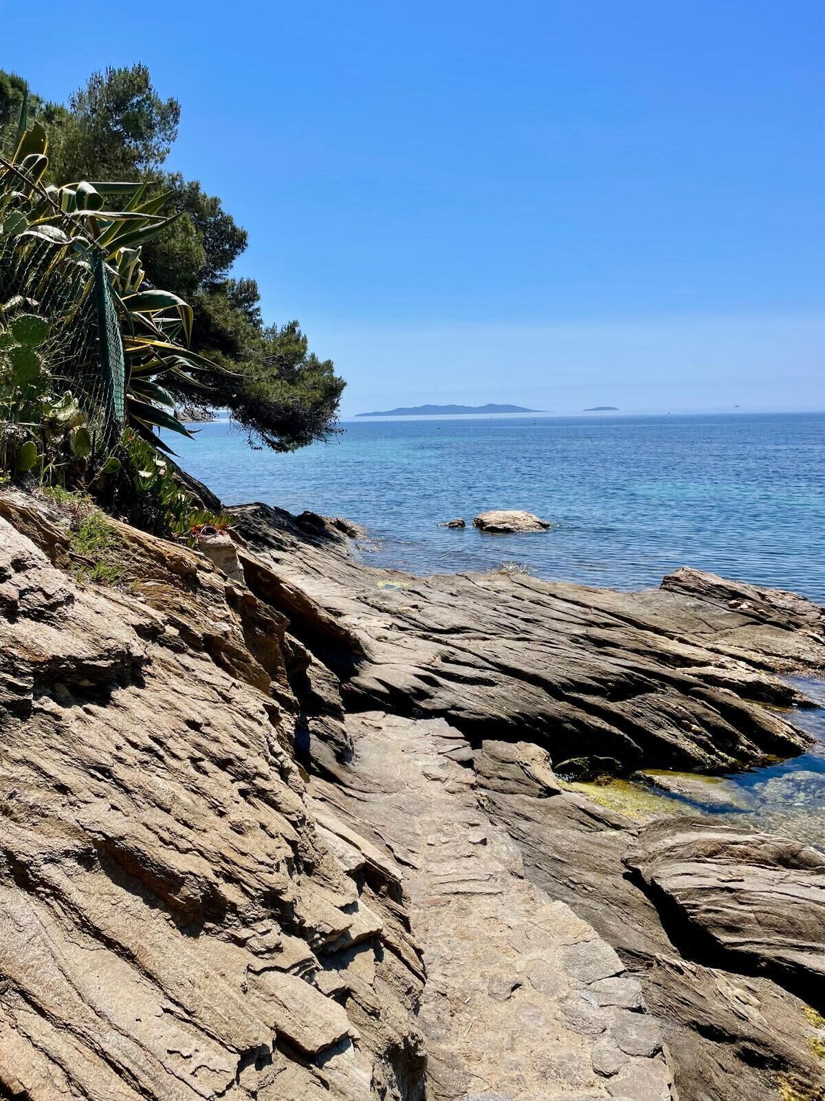 A rocky shoreline with clear blue water and distant islands.