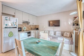 A compact kitchen with a dining area, a sofa, and a TV mounted on the wall. - Appartement avec jardin - Cavalière (Le Lavandou)