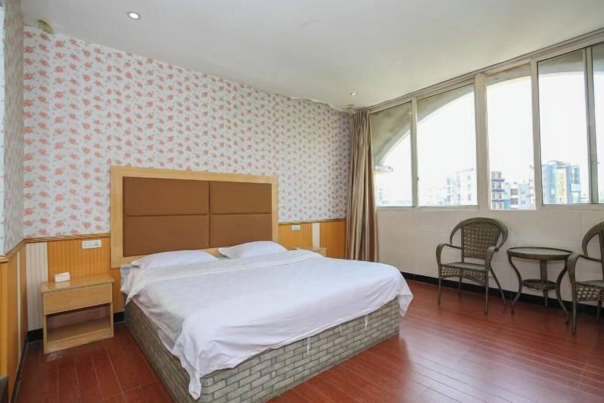 Habitación de hotel con cama, una mesita, dos sillas, ventana y vistas a la ciudad, además de un papel tapiz estampado.