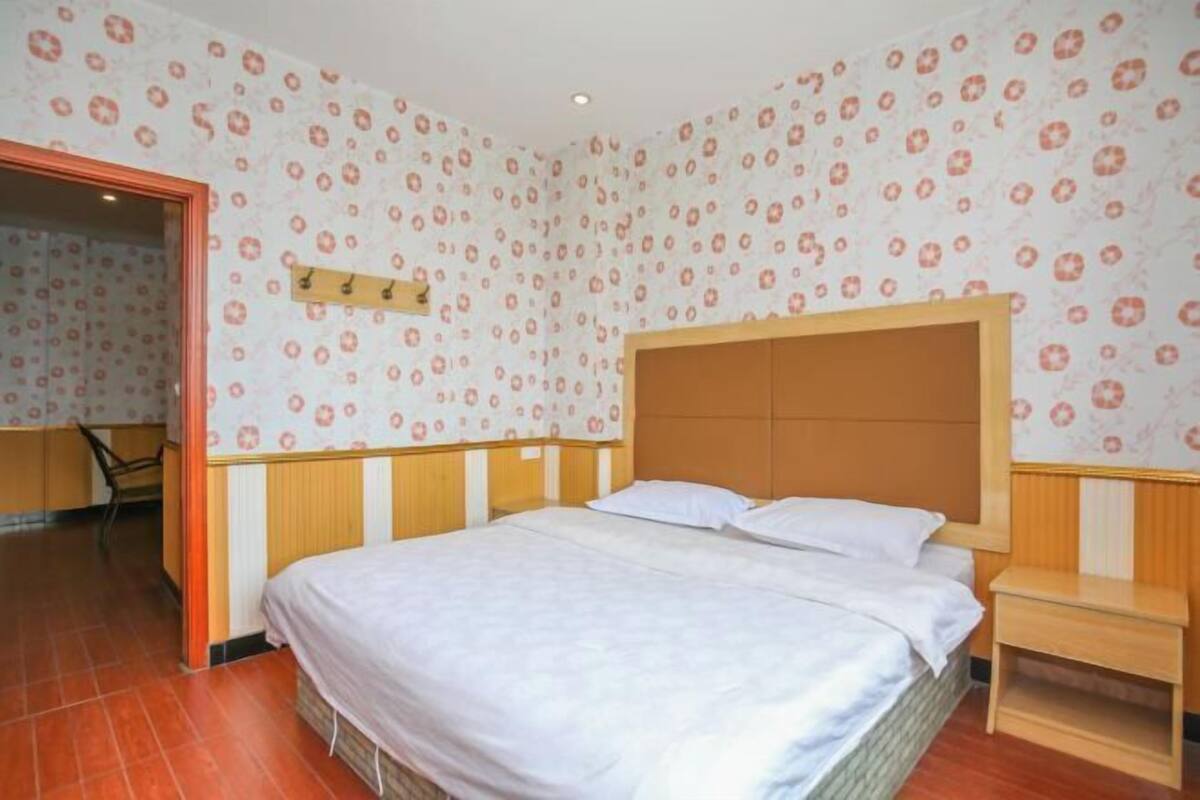 Un dormitorio con cabecera de madera, cama con ropa blanca, una mesita de noche pequeña y un estante montado en la pared.
