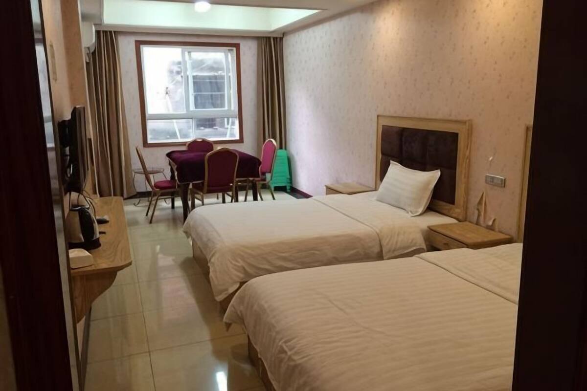 Habitación de hotel con dos camas, un escritorio con silla, televisión y ventana con cortinas.