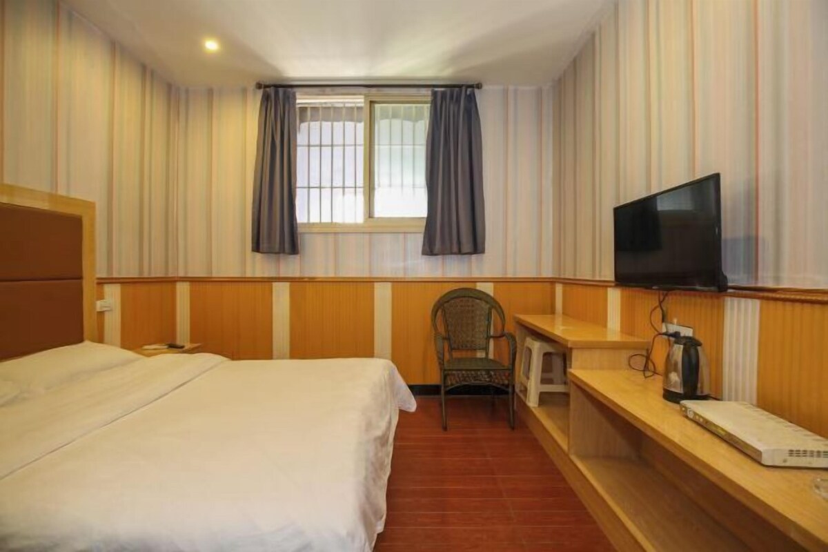 A hotel room with a bed, a desk with a television, a chair, and a window with curtains.