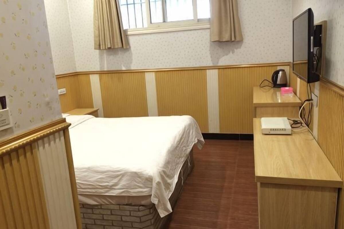 Un dormitorio con cama, escritorio, televisor y ventana con cortinas.