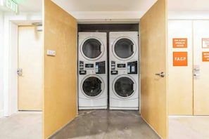 A laundry room with two front-loading washing machines, a fire alarm sign, and an exit sign.