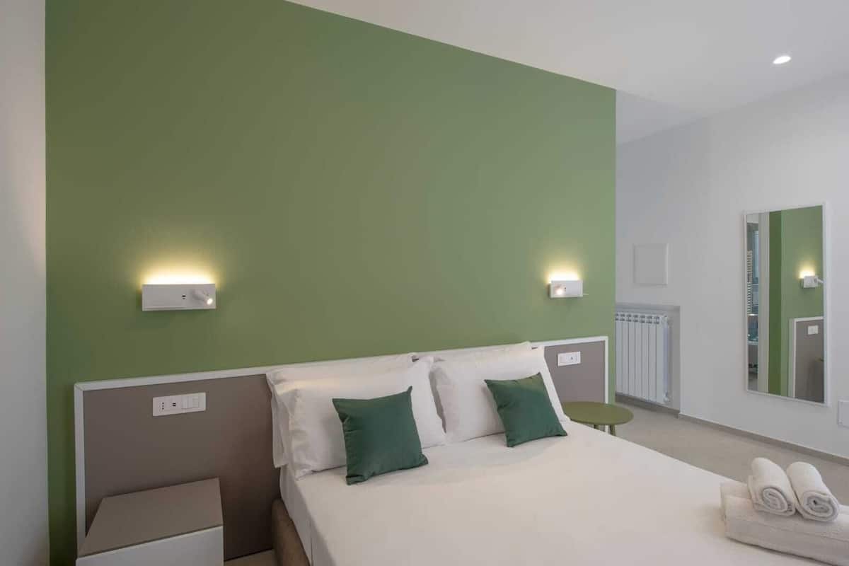 Une chambre d’hôtel avec un lit, deux tables de chevet, une table ronde, un miroir et des murs verts.