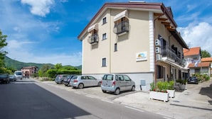 Un hotel a più piani con balconi, un parcheggio e montagne sullo sfondo.