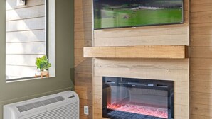 A living room with a fireplace, a mounted TV, and a window with blinds.
