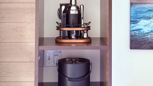 A kitchen area with a coffee maker, wine glasses, and a kettle on a shelf.