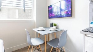 A modern dining area with a table and two chairs, a flat-screen TV mounted on the wall, and a window with blinds. - Condotel Broadway-E Jefferson-Close to Convention (Seattle)