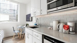 A modern kitchen with white cabinetry, a built-in microwave, and a coffee maker. - Cityscape-Condotel-First Hill (Seattle)