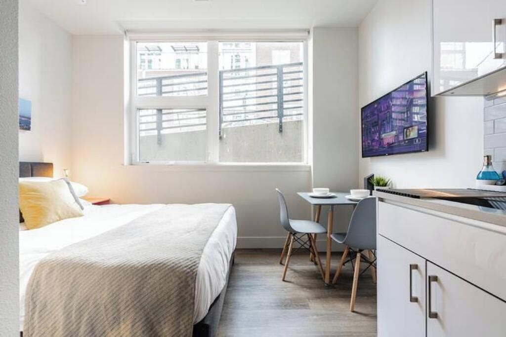 Ein modernes Hotelzimmer mit einem Bett, einem kleinen Schreibtisch, einem Sessel und einem an der Wand befestigten Fernseher.