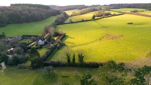 Un paysage rural avec une ferme, des champs et une zone boisée.