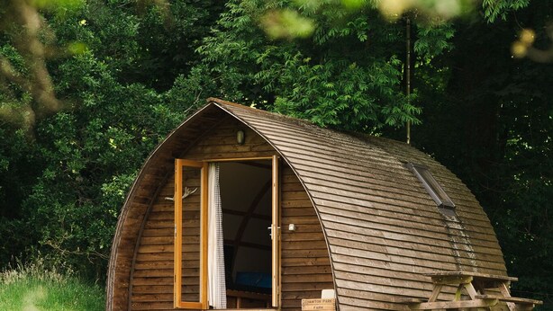 Une cabane en bois avec un toit incurvé, une grande porte ouverte et un petit espace porche.
