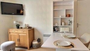 Ett modernt matområde med ett vitt bord dukat för två personer, ett träskåp och en tv som är monterad på väggen.