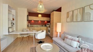 Ett kompakt bostadsutrymme med en matplats, ett litet kök och en sittgrupp med en soffa och ett soffbord.