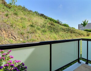 A balcony with a view of a hillside and a modern building in the background.