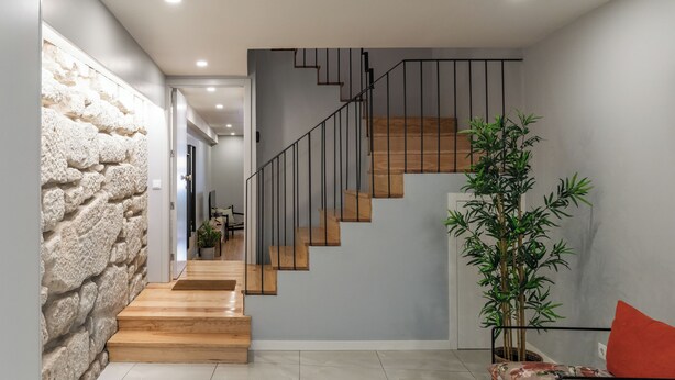 A modern interior with a staircase, a stone wall, a wooden floor, and a sofa with a cushion.