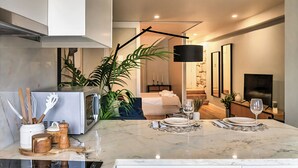 A modern kitchen with a marble countertop, a dining area with a table set for two, and a living room with a sofa and a TV.