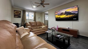 Uma sala de estar moderna com um sofá de couro, uma mesa de centro de vidro e uma TV de tela plana na parede.