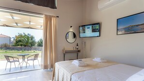A hotel room with a bed, a desk with a computer, a chair, and a view of the outdoors. - Apolithon Premium Houses (Lesvos)