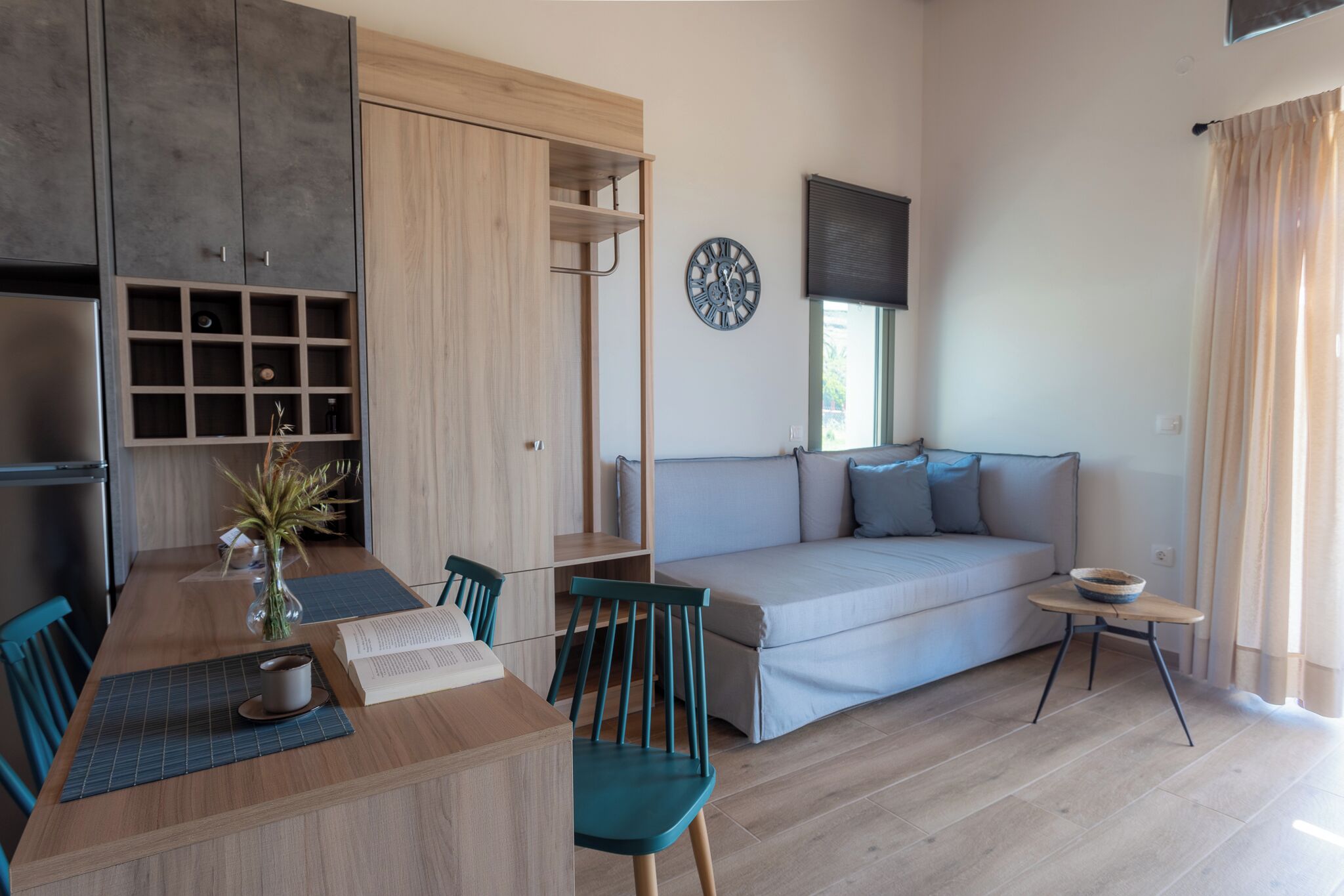 A modern living room with a wooden dining table, chairs, a sofa, and a small side table.