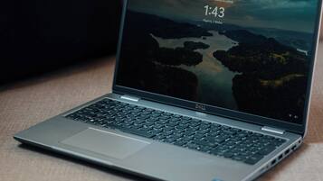 Una computadora portátil sobre un sofá con un cojín oscuro.