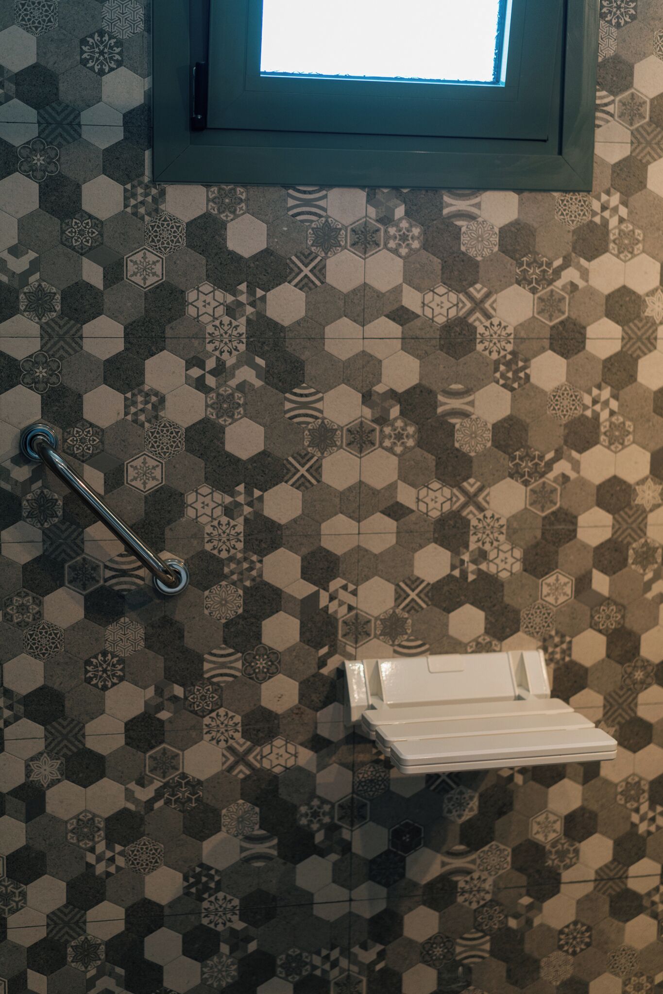 Un baño con piso de patrón hexagonal, un pasamanos y una ventana con vistas.
