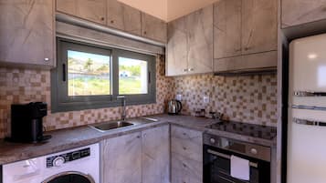 Eine kompakte Küche mit Waschmaschine, Kaffeemaschine, Wasserkocher und Kühlschrank.