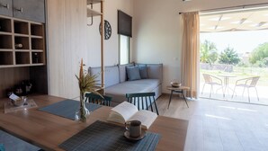 A modern room with a sofa, a dining table with a book and a cup, a small table with a bowl, and a view through a large window. - Apolithon Premium Houses (Lesvos)