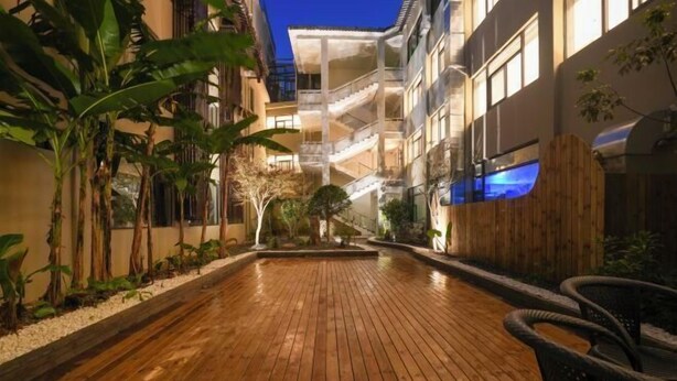 A wooden deck with a view of a multi-story building, surrounded by plants and a wooden fence. - Yandang Hotel (Wenzhou Teacher Education Institute Yandang) (Yueqing)