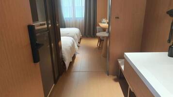 A hotel room with two beds, a small desk, a chair, and a window with curtains.