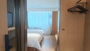 A hotel room with a bed, a bedside table, a hanging coat rack, and a window with curtains. - Yandang Hotel (Wenzhou Teacher Education Institute Yandang) (Yueqing)