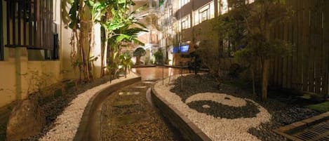 A pathway with a water feature, surrounded by plants and a wooden fence.