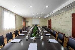 Un salón de conferencias con una larga mesa, sillas, una pantalla de proyector y una planta.