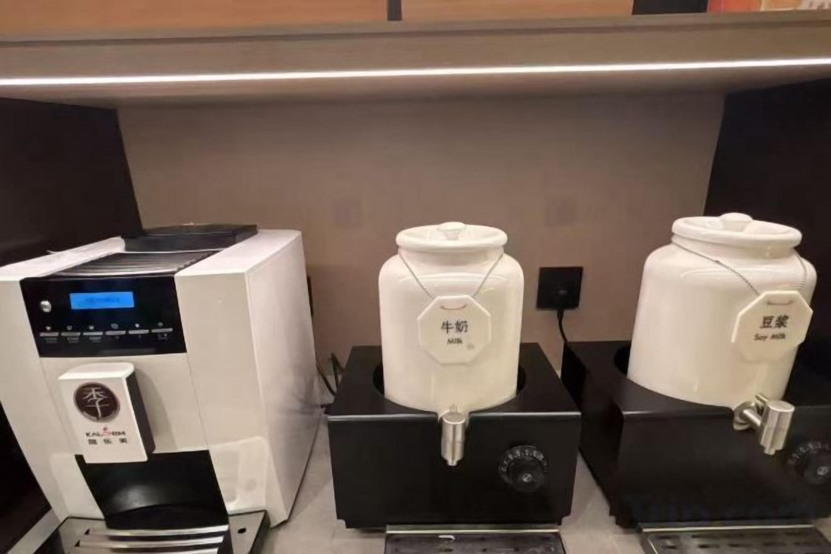 Máquina de café e dois dispensadores de leite de soja em um ambiente comercial.
