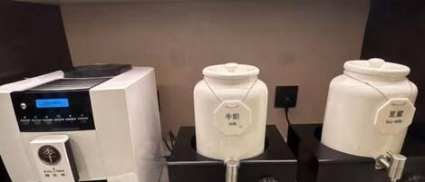 Máquina de café e dois dispensadores de leite de soja em um ambiente comercial.